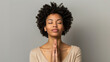 A serene individual with closed eyes is meditating, hands clasped together in a gesture of peace against a neutral background.