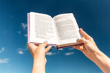 Fototapeta Przestrzenne - reading, education and knowledge concept - close up of hands holding open book over blue sky