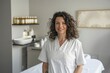 © TheosArtTavern - smiling woman in white medical gown standing infront bed looking into camera