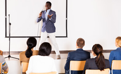 Canvas Print - Young emotional male motivation coach giving speech from speaker stage