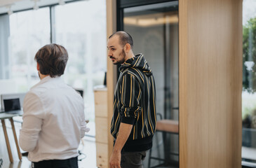 Two professional male colleagues engaged in discussion in a bright, contemporary office. The focus is on one looking back over his shoulder.