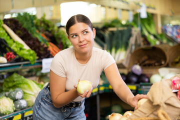 Canvas Print - Young woman shopper in casual clothes chooses onions in supermarket