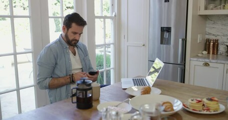 Wall Mural - Man, phone call and laptop in kitchen for morning online conversation at breakfast for business, planning or communication. Male person, digital device and coffee for email, internet or networking