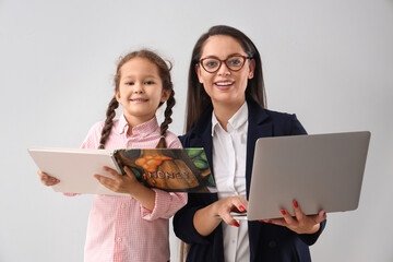 Wall Mural - Working mother with her little daughter reading book on light background