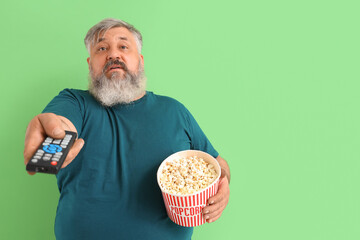 Canvas Print - Mature man with popcorn watching TV on green background