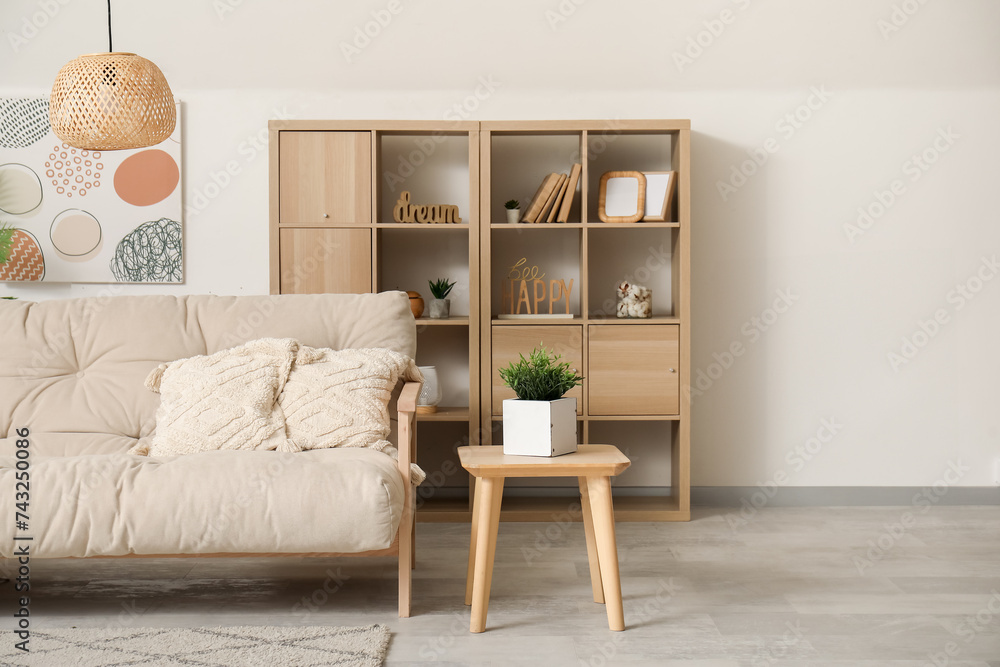 Interior of light living room with comfortable sofa, shelves and table