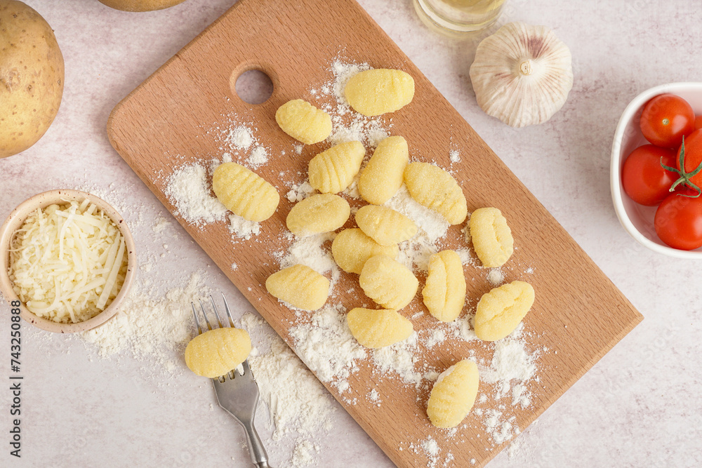Wooden board with tasty gnocchi and tomatoes on light background