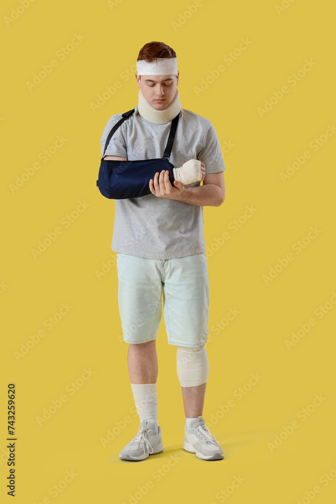 Injured young man after accident with broken arm on yellow background