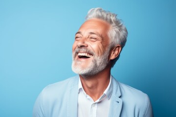 Wall Mural - Cheerful senior man is laughing and looking at camera. Isolated on blue background