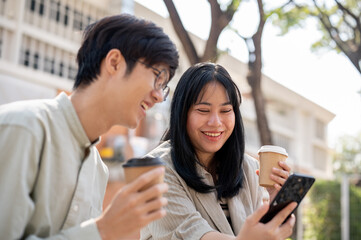 Wall Mural - Two friends are enjoying talking, watching videos on a phone together while chilling in a park.