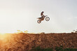 Person, jump and motorcyclist in the air on mockup with sunset for trick, stunt or ramp on outdoor dirt track. Expert rider on motorbike with lift off for extreme sports or rally challenge in nature