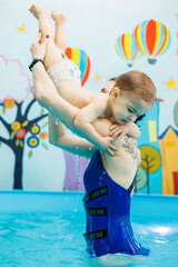 Wall Mural - A little boy is swimming in the pool with a coach. Teaching children to swim. Children's swimming school