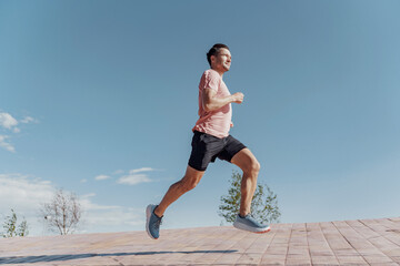 Runner in motion against a clear blue sky, focus on fitness and health, enjoying outdoor workout on a bright sunny day.