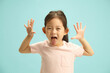 Playful and Lovely Asian Ethnicity Child Girl cheerfully showing opening hands up, sticking out tongue, expresses joyful mood standing against blue isolated. Concept of children happy.