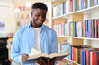A young man stands confidently in a library, surrounded by shelves of books, embodying the pursuit of knowledge.