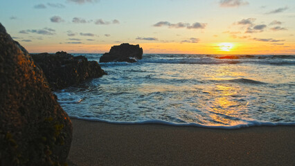 Poster - Beautiful natural landscape with sandy beach  with big stones during sunset.  Sun over horizon and Rolling ocean waves to the rocky shore while sunset.  Summer tourist destination in Portugal. Travel