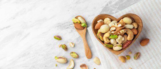 Wall Mural - Nuts mixed in heart wood bowl on marble table background with linen cloth, top view