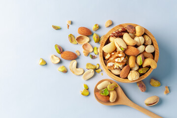 Wall Mural - Nuts mixed in wooden bowl with spoon on blue background, top view