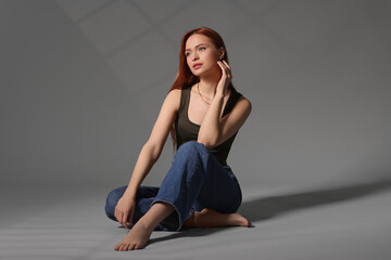 Wall Mural - Beautiful young woman sitting on gray background