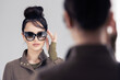 © Valua Vitaly - Beautiful brunette woman  in sunglasses poses in front of a mirror. Young adult girl in stylish black sunglasses. Fashion and beauty concept.
