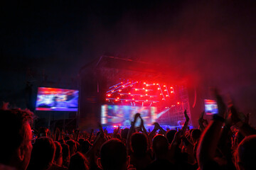 Wall Mural - Image shot during a music festival. Light comes from a stage with a band show, people silhouettes are visible in front of it.