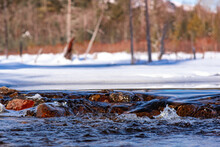 Water Flowing Over Rocks On Partially Frozen NH Pond Background Of Snow