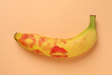 Wall Mural - Banana with red lipstick marks on pale orange background, top view. Sex concept