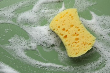 Yellow sponge with foam on green background, top view