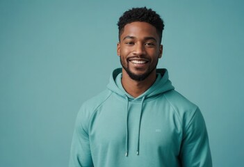 Man in a hooded sweatshirt smiles warmly, with a blue background that complements his relaxed style. His casual pose suggests comfort and ease.