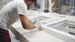 In a focused close-up view, a worker installs a plastic window indoors, their hands skillfully maneuvering the frame into place, ensuring a tight seal and flawless finish to the installation process.