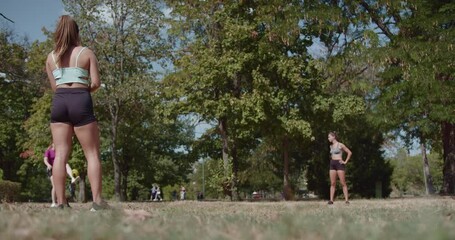 Wall Mural - Three athletic women stand ready on a grassy field in the park, about to start their running workout on a bright, sunny day.