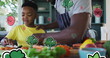 Image of vegetables floating over happy african american father and son preparing meal