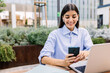 © Xavier Lorenzo - Young business woman writing message on mobile phone while working on laptop sitting outside of office building.
