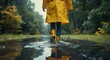A fashion-forward individual stands gracefully under a tree, sporting a vibrant yellow raincoat and boots, embracing the outdoor elements as they walk through a puddle of water with confidence and st