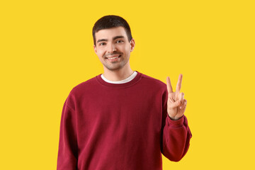 Canvas Print - Young man showing victory gesture on yellow background