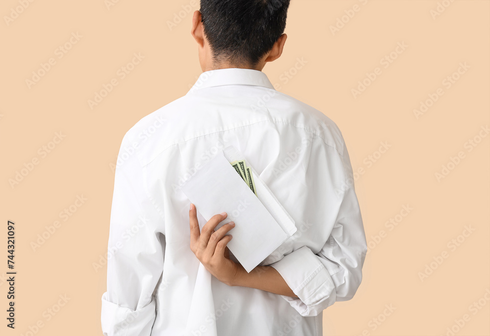 Young Asian man with envelope of money on beige background, back view