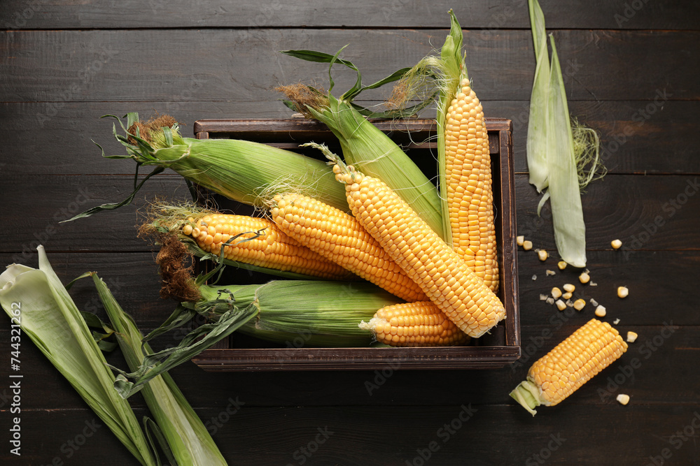 Box with fresh corn cobs on wooden background