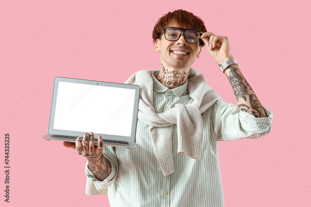 Handsome young tattooed businessman with laptop on pink background