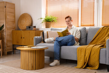 Wall Mural - Redhead young happy man reading book on sofa at home