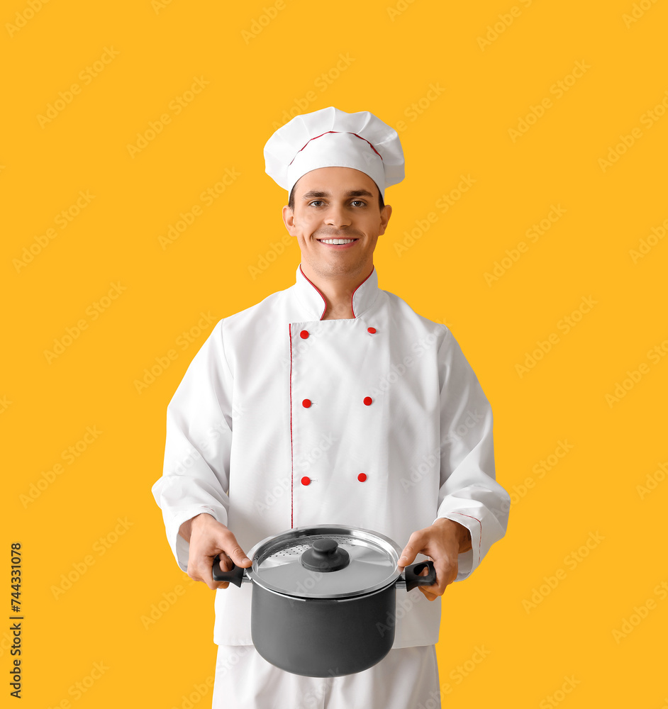 Handsome happy male chef with cooking pot on yellow background