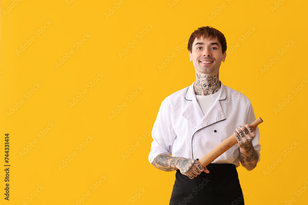 Tattooed happy male chef with rolling pin on yellow background
