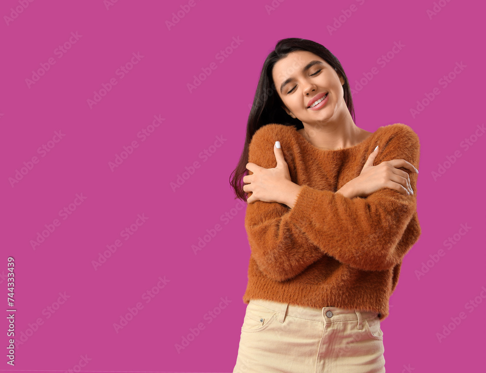 Beautiful young happy woman hugging herself on purple background