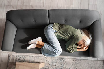 Sticker - Depressed mature woman lying on sofa at home, top view