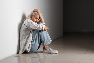 Poster - Depressed mature woman sitting near wall in dark hall