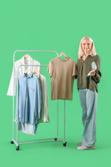 Sticker - Happy mature woman with modern garment steamer and clothes on green background