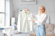 © Pixel-Shot - Happy mature woman steaming shirt with modern garment steamer at home