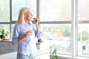 Sticker - Mature woman with glass of water taking pills in kitchen