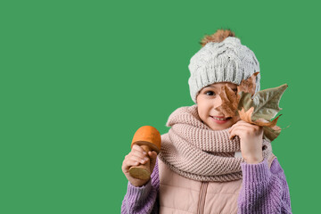 Wall Mural - Cute little happy girl in warm clothes with autumn leaf and mushroom on green background