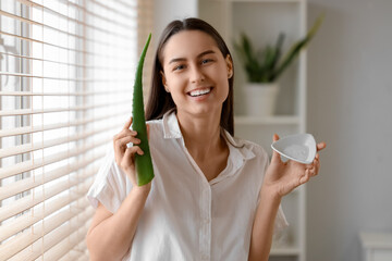 Wall Mural - Beautiful young woman with plate of aloe vera gel near window at home