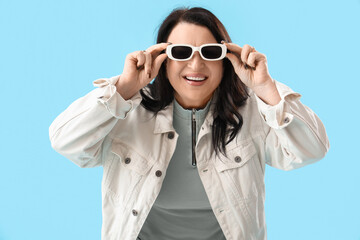 Wall Mural - Beautiful happy mature woman in stylish sunglasses on blue background. International Women's Day